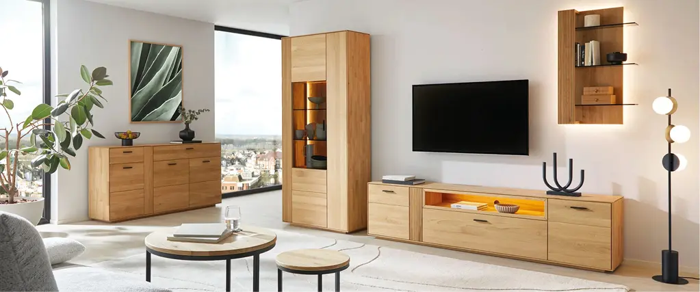 Helles Wohnzimmer mit TV-Board, Vitrine und Sideboard aus Massivholz. Moderne Wohnmöbel im natürlichen Design mit Glasfront und Beleuchtung, kombiniert mit Couchtisch und großem Teppich für stilvolles Wohnen.